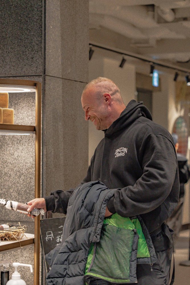 Hugh in a Zen Den Studios hoodie laughing while examining products at a Tokyo retail display — Zen Den Studios