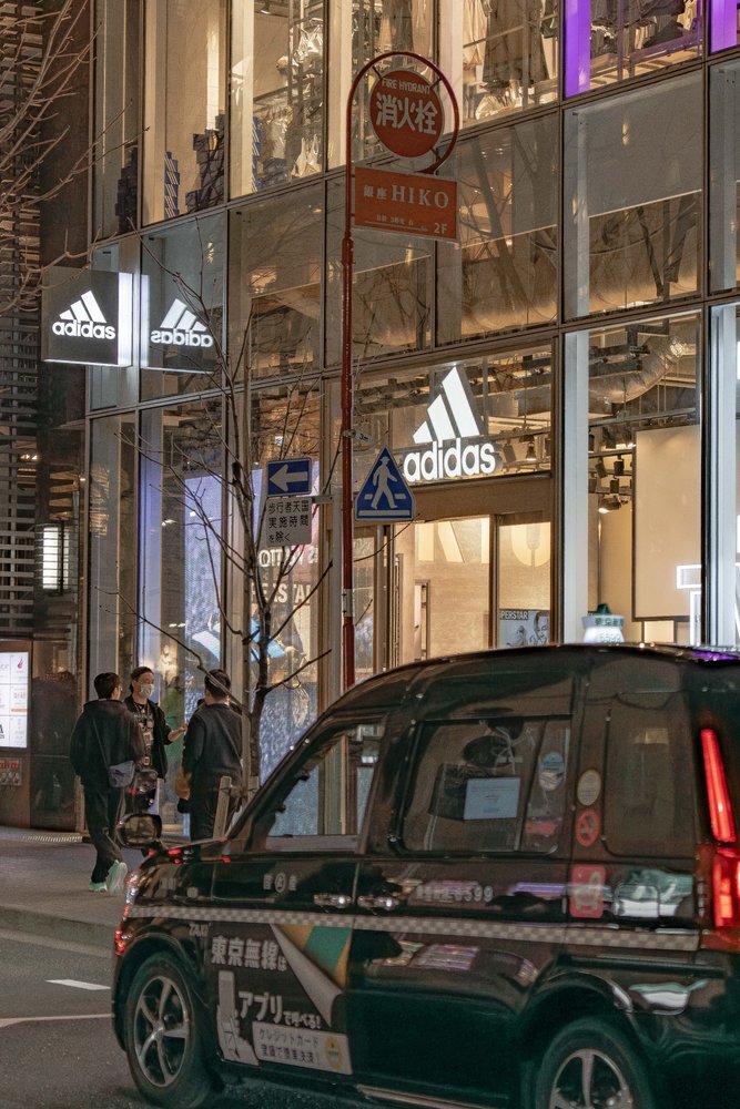 Adidas store at night in Tokyo with a taxi in the foreground and pedestrians on the street — Zen Den Studios