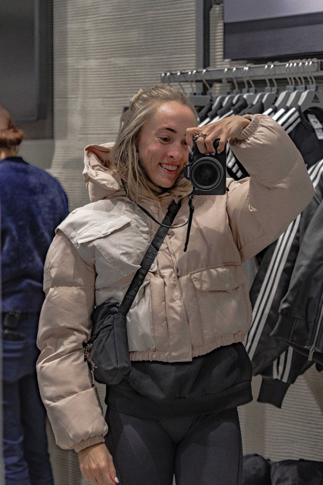 Liz smiling and raising a camera to her face inside an Adidas store in Tokyo — Zen Den Studios