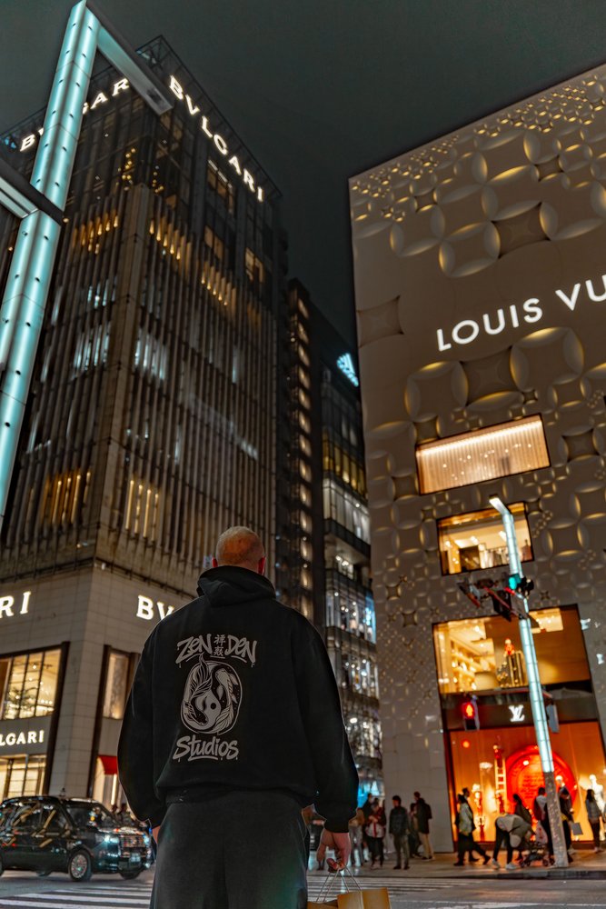 Hugh in a Zen Den Studios hoodie standing in front of the Bvlgari and Louis Vuitton buildings in Ginza at night — Zen Den Studios