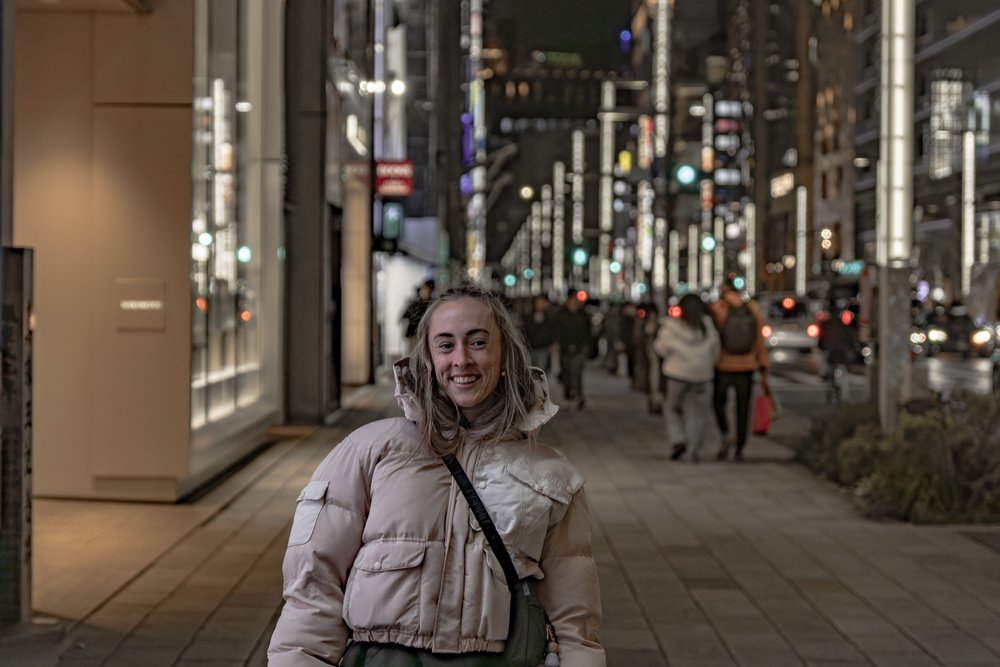 Liz smiling on a lit-up Ginza street at night with bokeh city lights stretching behind her — Zen Den Studios