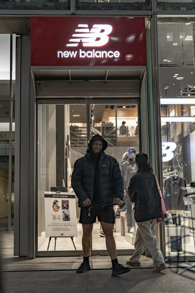 Hugh standing at the entrance of a New Balance store on a Tokyo street at night — Zen Den Studios