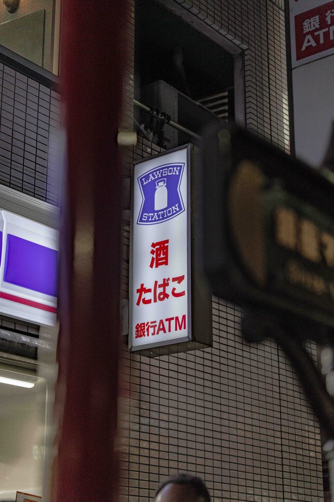Illuminated Lawson Station sign at night in Tokyo with Japanese text — Zen Den Studios